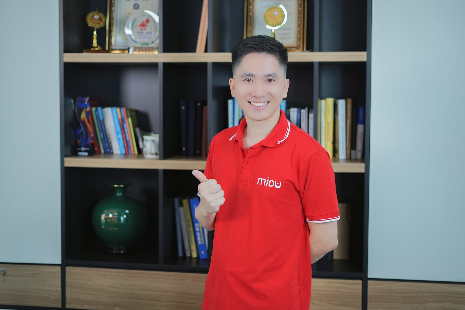 Nguyễn Xuân Hợp giơ ngón cái trước tủ sách