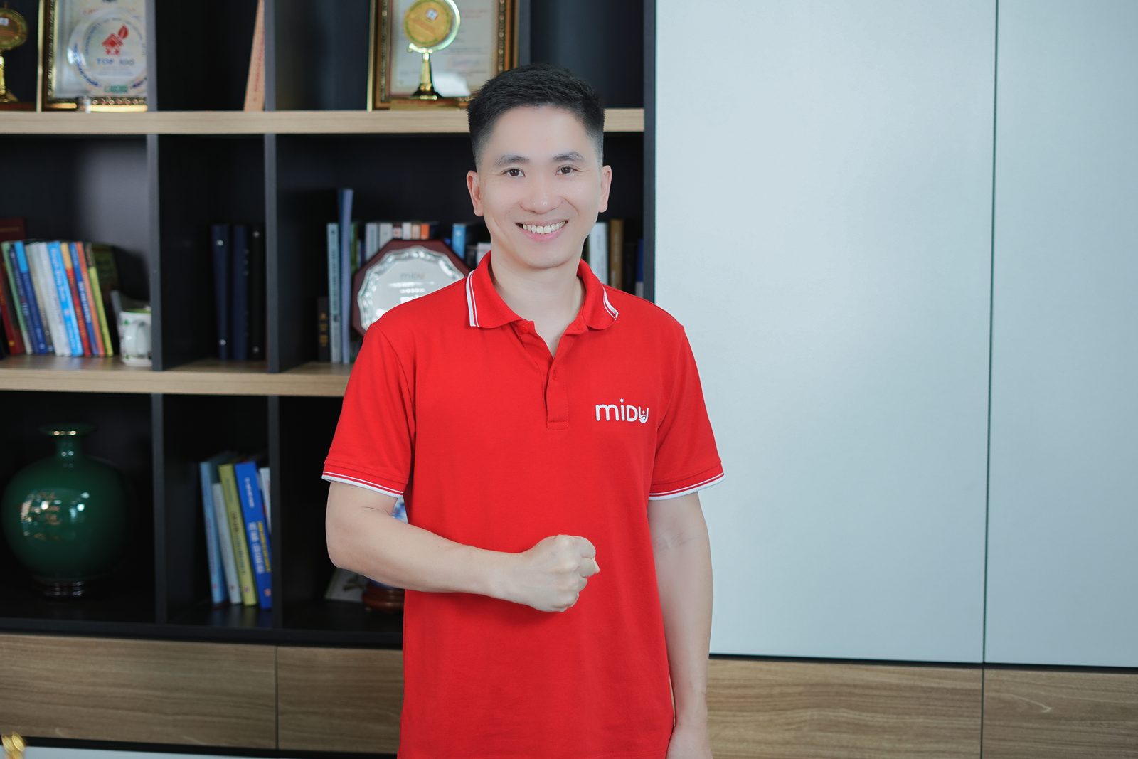 Nguyễn Xuân Hợp đứng trước tủ sách và cúp trong phòng làm việc